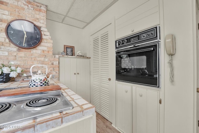 kitchen featuring tile counters, oven, a paneled ceiling, brick wall, and stovetop