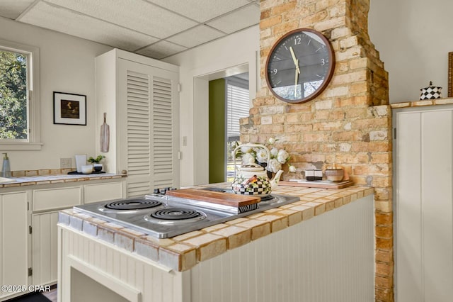 kitchen featuring tile counters, white cabinets, a drop ceiling, and stainless steel gas cooktop