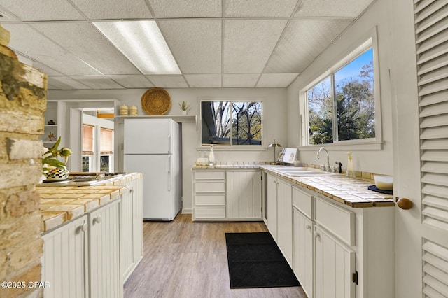 kitchen featuring white fridge, tile counters, white cabinetry, and sink