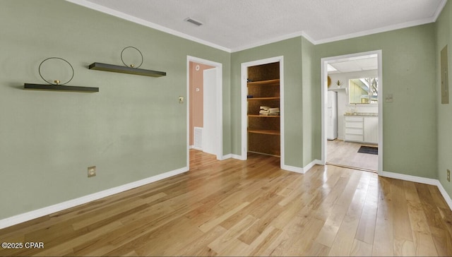 empty room featuring light hardwood / wood-style floors, built in shelves, ornamental molding, and a textured ceiling