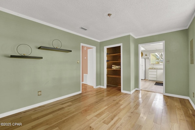 empty room featuring light wood-type flooring, ornamental molding, and a textured ceiling