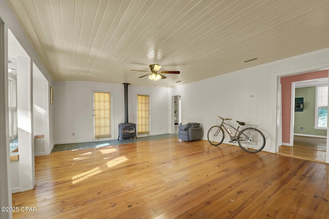 unfurnished living room with ceiling fan, wooden ceiling, a wood stove, and hardwood / wood-style floors