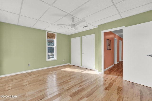 spare room featuring light wood-type flooring, ceiling fan, and a drop ceiling