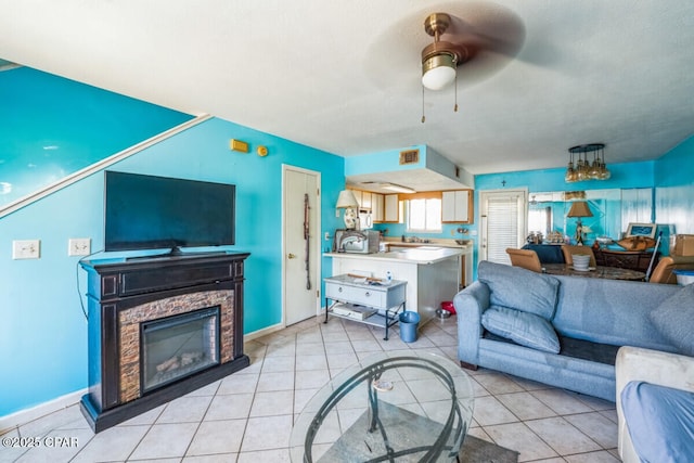 tiled living room with ceiling fan and a stone fireplace