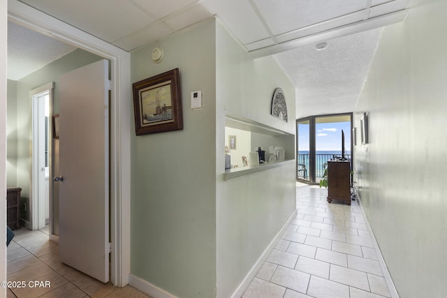 hall with a water view, expansive windows, light tile patterned flooring, and a textured ceiling