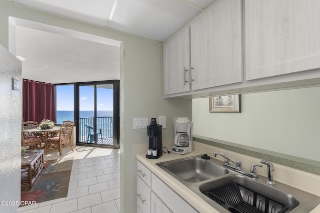 kitchen with light tile patterned floors, sink, a wall of windows, and a water view