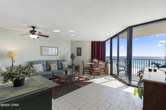 living room with a textured ceiling, a water view, ceiling fan, light tile patterned floors, and expansive windows