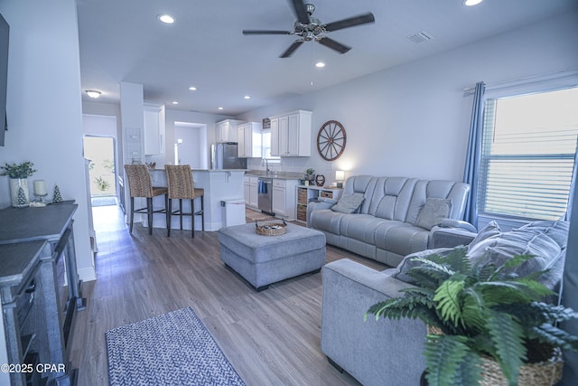 living room featuring light wood-type flooring, ceiling fan, and sink