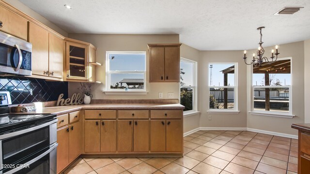 kitchen with decorative light fixtures, a textured ceiling, appliances with stainless steel finishes, a notable chandelier, and light tile patterned flooring