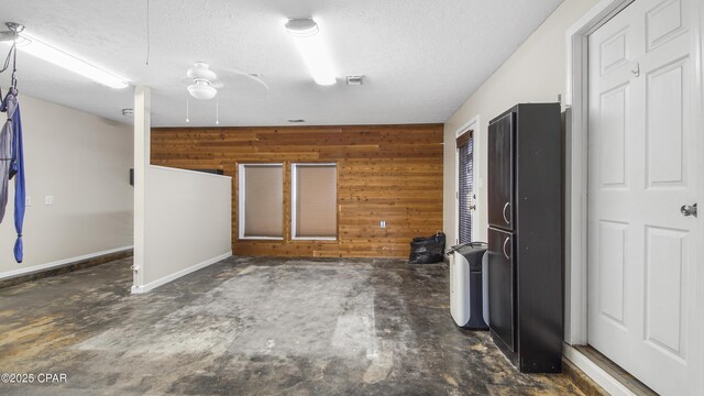 interior space with a textured ceiling, ceiling fan, and wood walls