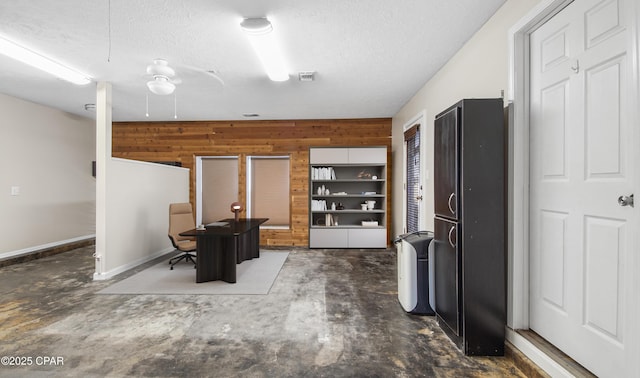 kitchen with ceiling fan, wood walls, concrete flooring, and a textured ceiling