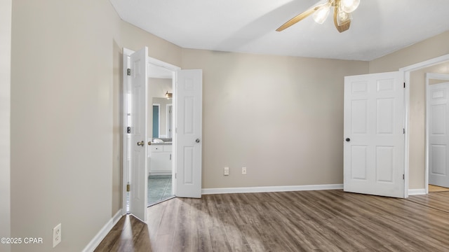 unfurnished bedroom featuring ensuite bath, baseboards, and wood finished floors