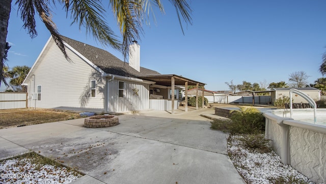 rear view of property featuring roof with shingles, a patio, a chimney, fence, and a fire pit