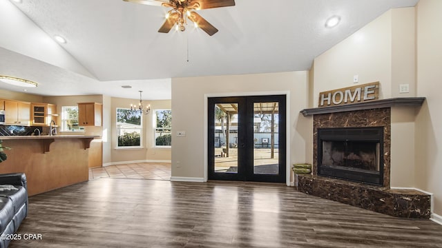 living room featuring vaulted ceiling, a premium fireplace, dark hardwood / wood-style flooring, and ceiling fan with notable chandelier