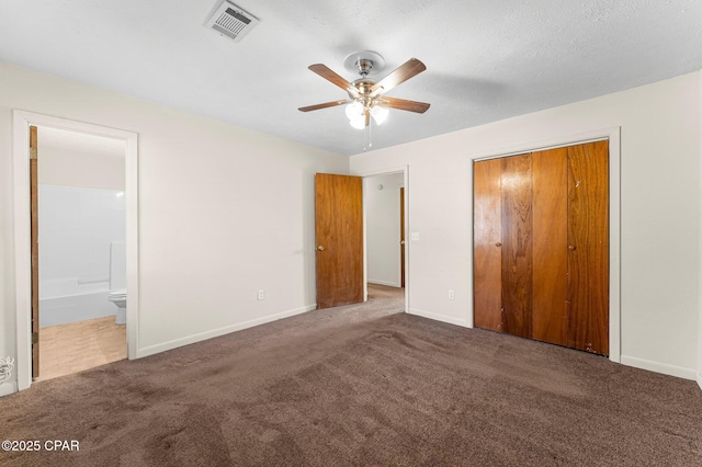 unfurnished bedroom with dark colored carpet, ceiling fan, ensuite bath, and a closet