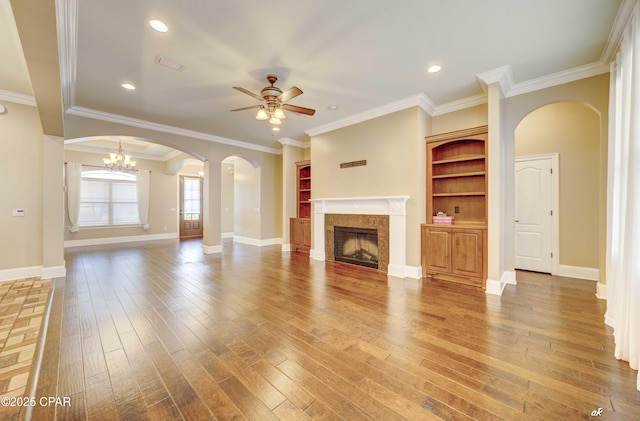 unfurnished living room featuring hardwood / wood-style floors, ceiling fan with notable chandelier, ornamental molding, and built in shelves