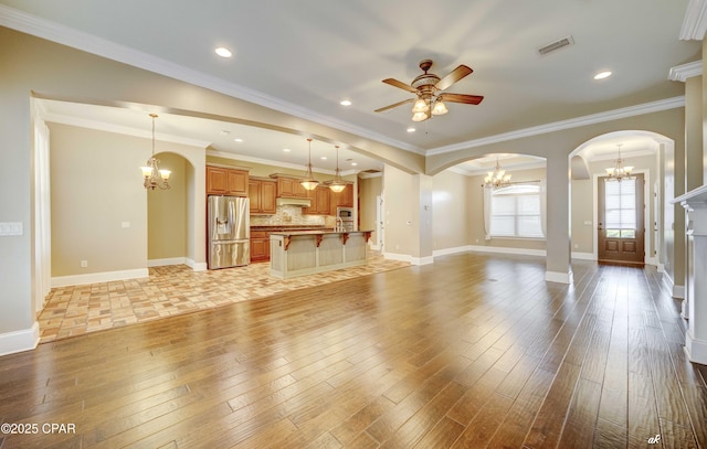 unfurnished living room with ornamental molding, ceiling fan with notable chandelier, and light wood-type flooring