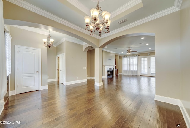 unfurnished living room featuring crown molding, dark wood-type flooring, ceiling fan with notable chandelier, and a tray ceiling