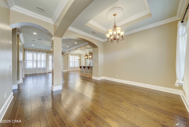 empty room featuring crown molding, wood-type flooring, a raised ceiling, and ceiling fan with notable chandelier