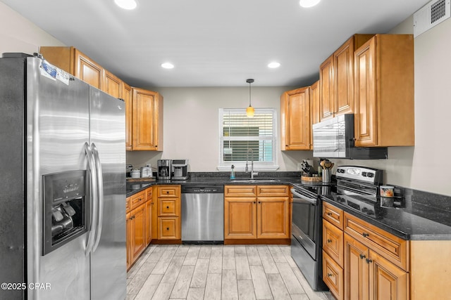 kitchen with appliances with stainless steel finishes, sink, dark stone countertops, and decorative light fixtures