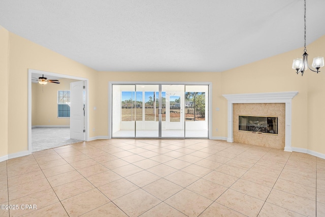 unfurnished living room with lofted ceiling, a high end fireplace, ceiling fan with notable chandelier, light tile patterned floors, and a textured ceiling