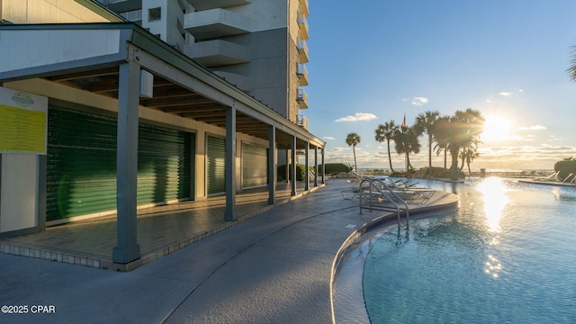 pool at dusk with a patio area and a water view