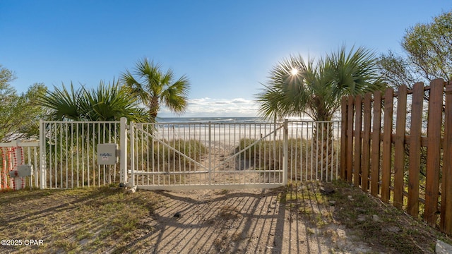 view of gate with a water view and a beach view