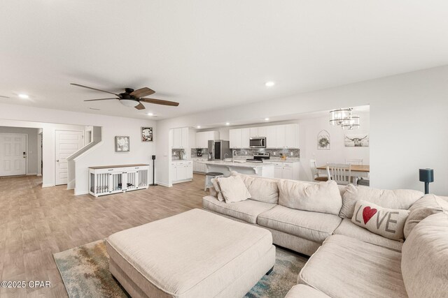 living room with ceiling fan with notable chandelier and light hardwood / wood-style floors