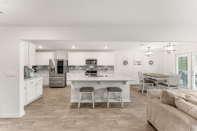 kitchen featuring an island with sink, hanging light fixtures, white cabinets, and stainless steel appliances