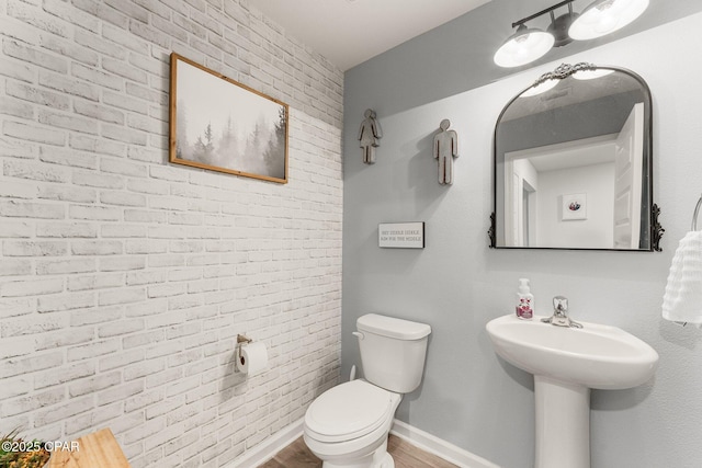 bathroom featuring wood-type flooring, toilet, and brick wall