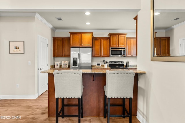 kitchen with a kitchen breakfast bar, ornamental molding, appliances with stainless steel finishes, light hardwood / wood-style floors, and light stone counters