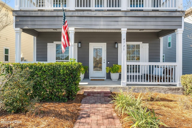 view of exterior entry featuring a balcony and covered porch