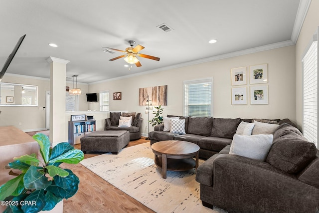 living room featuring light wood-type flooring, ornate columns, ceiling fan, and crown molding