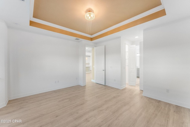 empty room with crown molding, light wood-style floors, and a tray ceiling