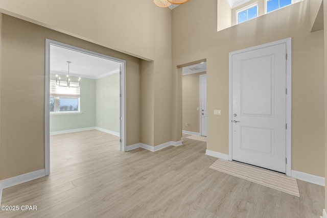 foyer entrance with baseboards, a notable chandelier, plenty of natural light, and light wood finished floors