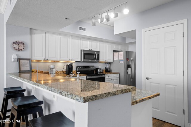 kitchen with white cabinetry, stainless steel appliances, light stone counters, kitchen peninsula, and a breakfast bar