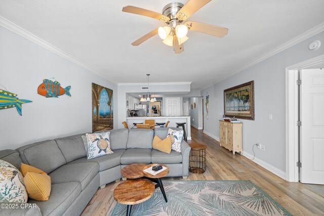 living room with crown molding, ceiling fan with notable chandelier, and light wood-type flooring