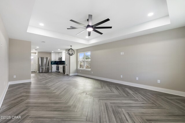 unfurnished living room with a tray ceiling and ceiling fan with notable chandelier