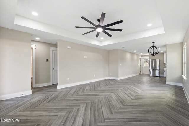 unfurnished living room with a raised ceiling and ceiling fan with notable chandelier