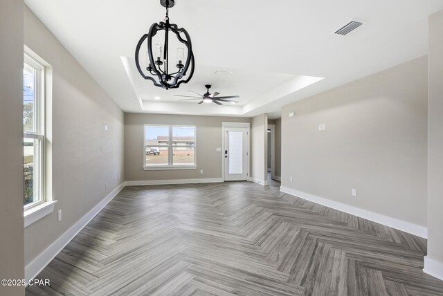 unfurnished living room with ceiling fan with notable chandelier and a tray ceiling