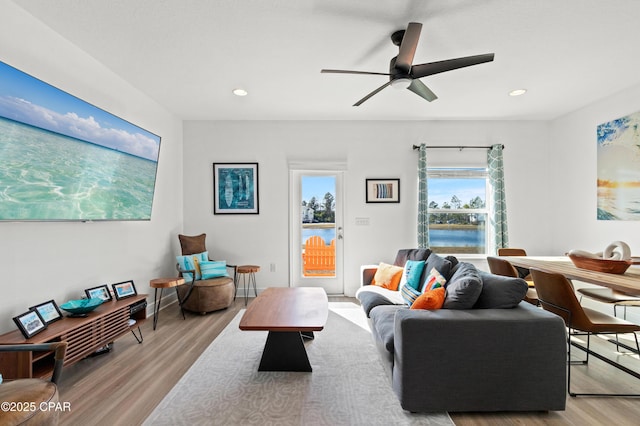 living room with ceiling fan, a water view, and light wood-type flooring