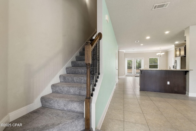 staircase with ornamental molding, a textured ceiling, tile patterned floors, french doors, and a chandelier