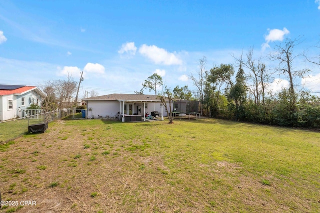 rear view of property featuring a trampoline, fence, and a lawn