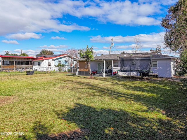 back of property with a trampoline, fence, and a lawn