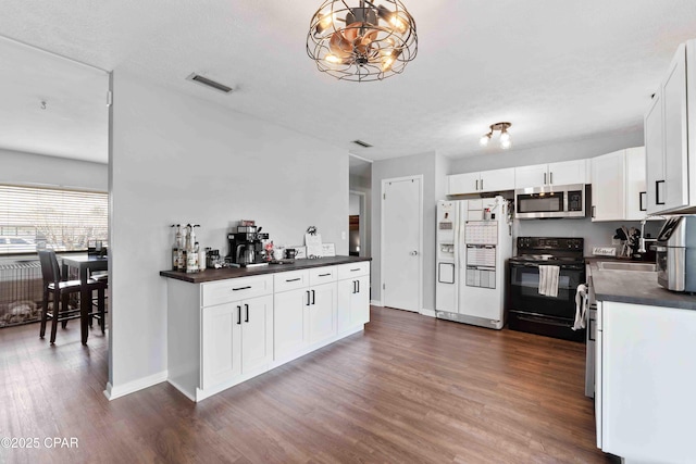 kitchen featuring black range with electric cooktop, white refrigerator with ice dispenser, white cabinetry, stainless steel microwave, and dark countertops