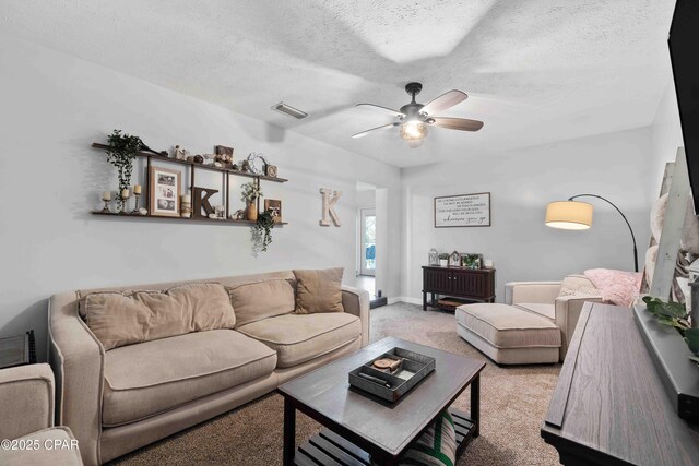 living area featuring a textured ceiling, light colored carpet, a ceiling fan, baseboards, and visible vents