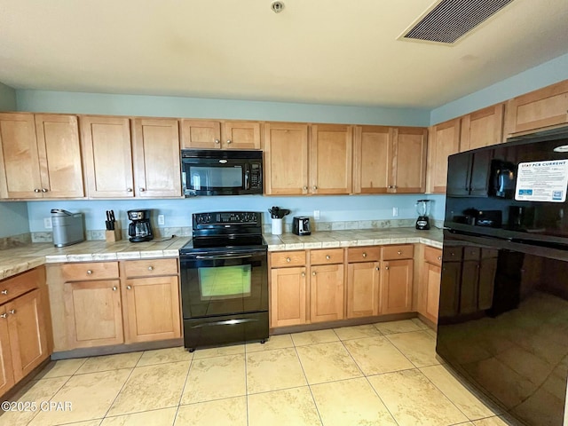 kitchen with black appliances, light tile patterned floors, and tile countertops