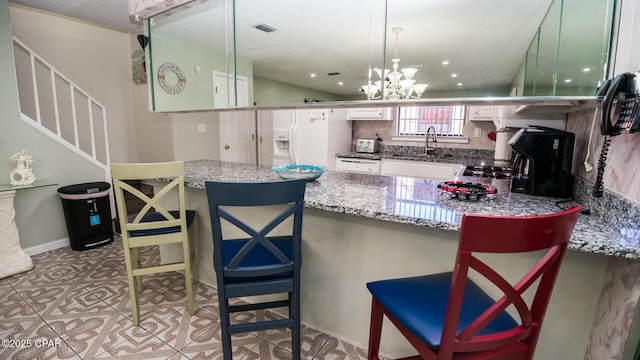 kitchen featuring sink, an inviting chandelier, white refrigerator with ice dispenser, decorative light fixtures, and a breakfast bar area