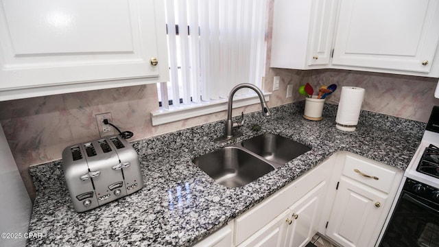 kitchen featuring dark stone countertops, white cabinetry, sink, and tasteful backsplash