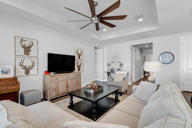 living room with a raised ceiling, ceiling fan, and light hardwood / wood-style floors